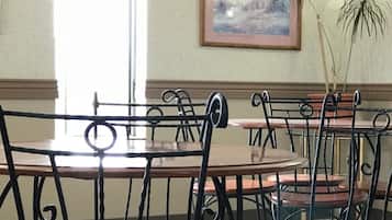 A dining area with round tables and chairs, a framed picture on the wall, and a potted plant.