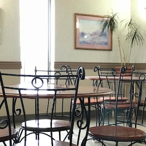 Uma área de refeições com mesas e cadeiras redondas, um quadro na parede e um vaso com planta.
