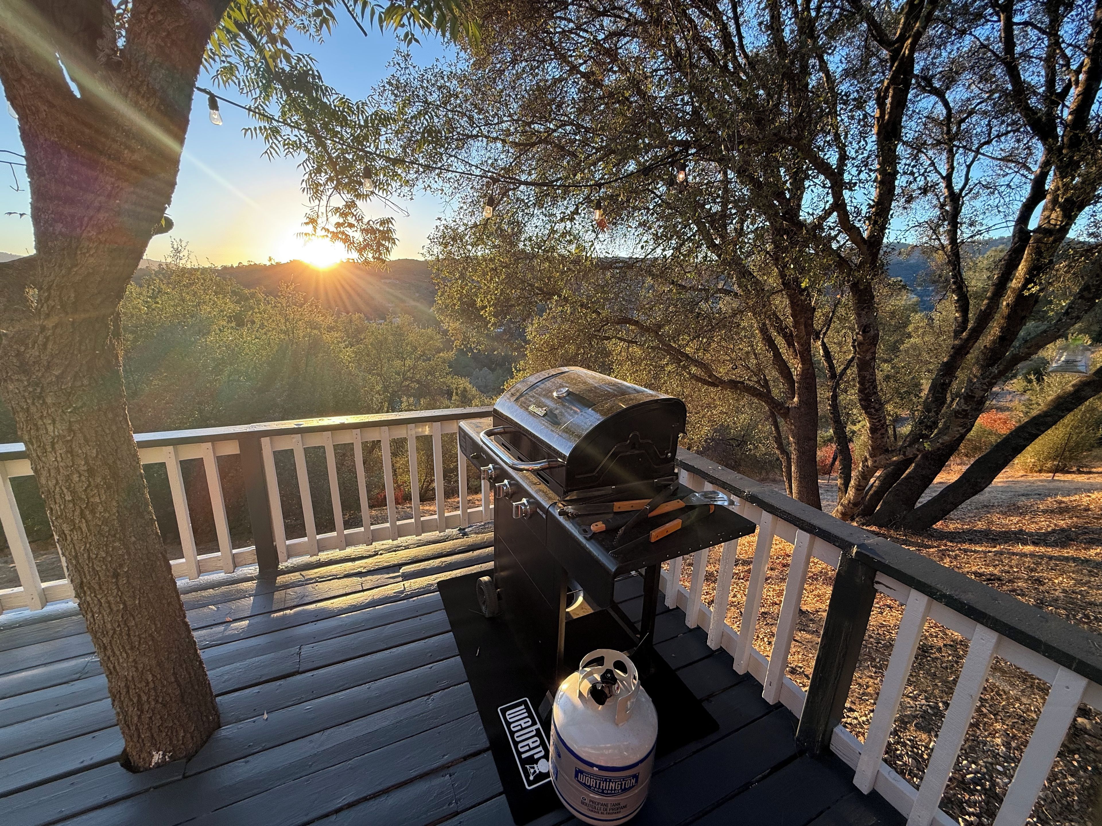 A deck with a barbecue grill and propane tank, surrounded by trees and a view of the landscape.