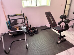 Une salle de sport équipée de matériel d’exercice, notamment un banc, des haltères et un support à poids.