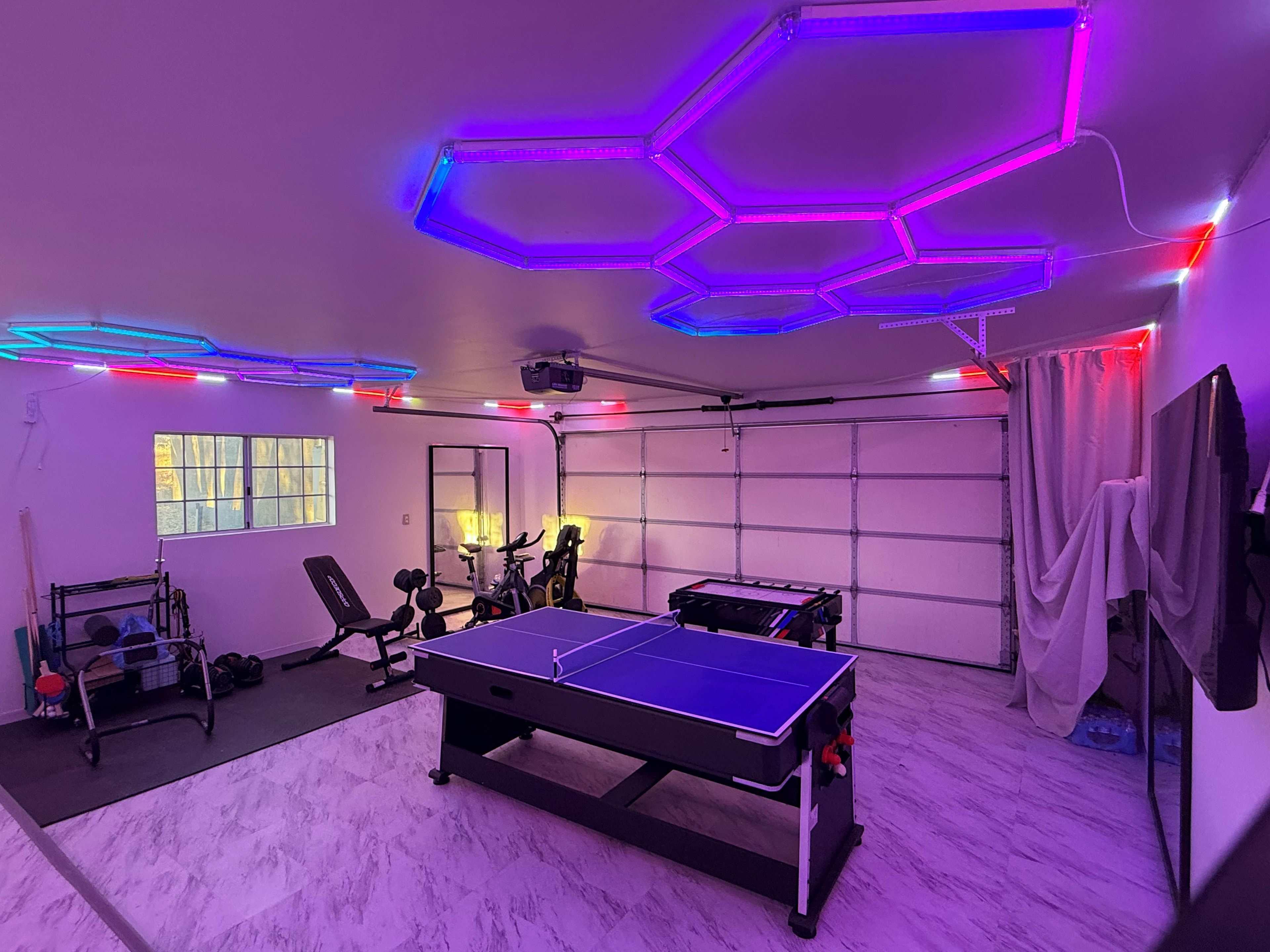 A room with a ping pong table, exercise equipment, and a garage door.