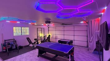 A room with a ping pong table, exercise equipment, and a garage door.