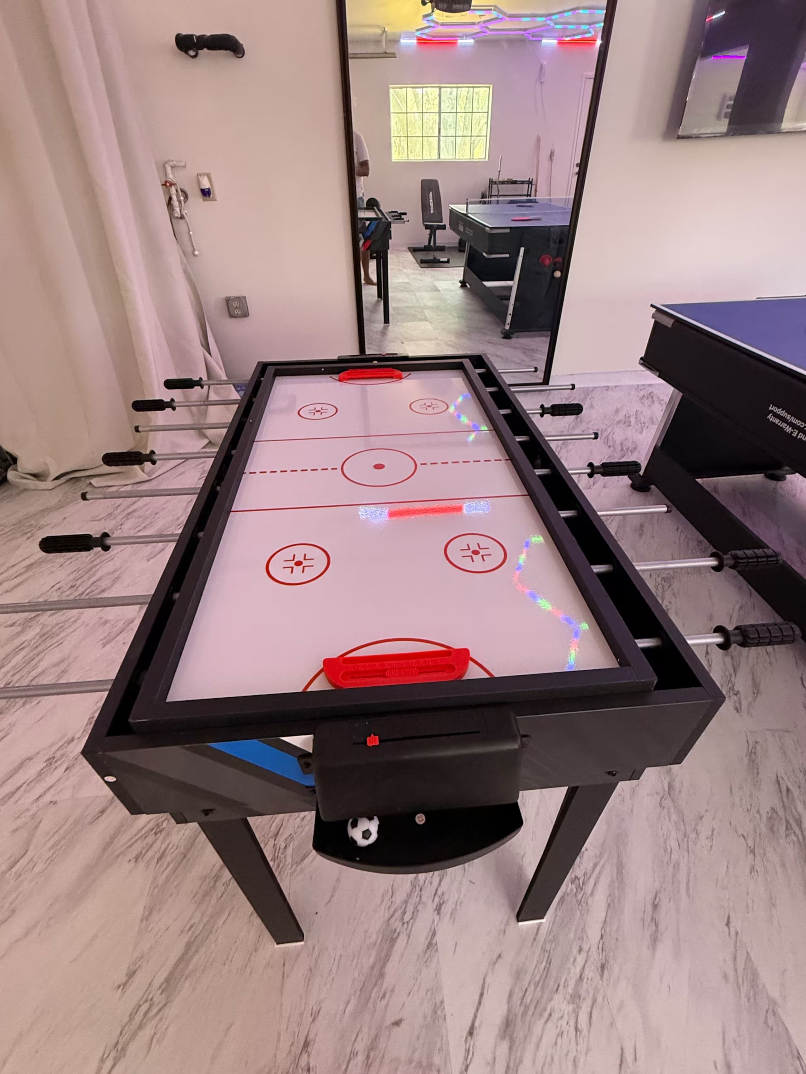 A foosball table with a clear view of the room layout, including a desk and a piano in the background.