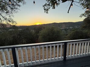 Une vue depuis un balcon doté d’une balustrade blanche, donnant sur un paysage arboré avec une ville visible au loin.