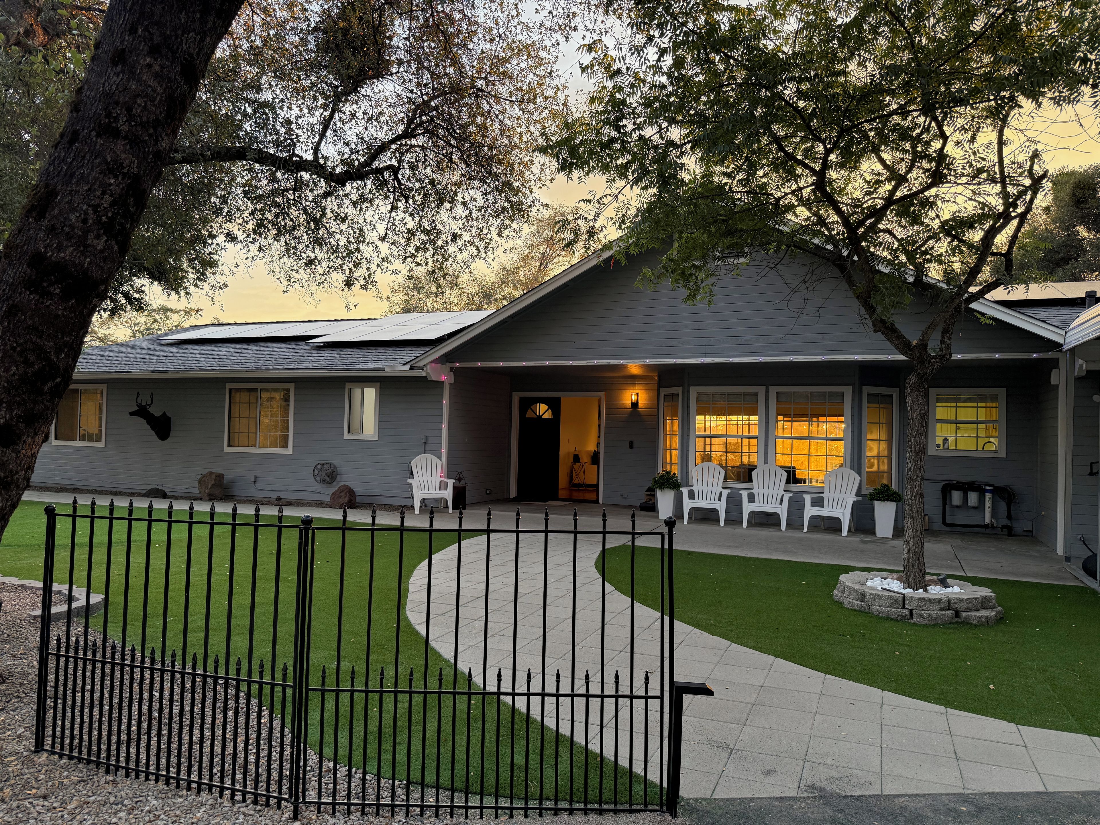 A residential house with a front porch, a fenced yard, and a tree.
