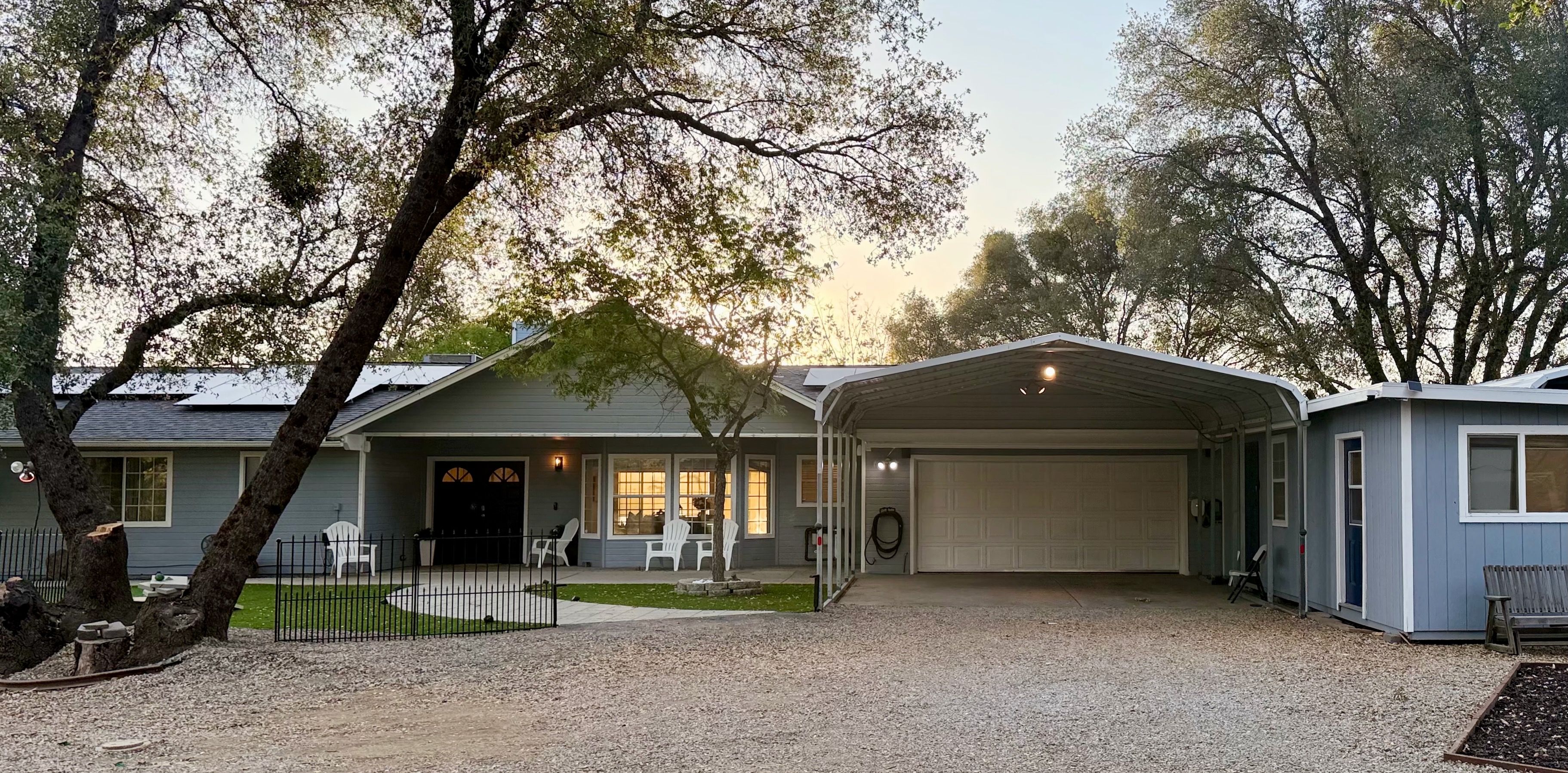 Une maison à deux étages avec un garage fermé, une véranda à l’avant avec des chaises et une allée gravillonnée.