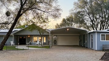 Une maison à deux étages avec un garage fermé, une véranda à l’avant avec des chaises et une allée gravillonnée.
