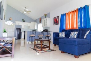 A living room with a blue sofa, a coffee table, and a dining area with chairs and a table. - The Oasis Golf Retreat (Kingston)