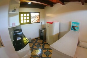 Cozinha compacta com fogão, pia e geladeira. Há uma janela com vista para uma escada e uma porta.