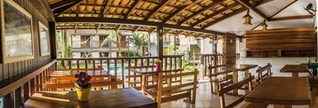 Restaurante com móveis de madeira, vista para a piscina e área de estar coberta ao ar livre.