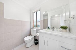Een moderne badkamer met toilet, wastafel en spiegel.