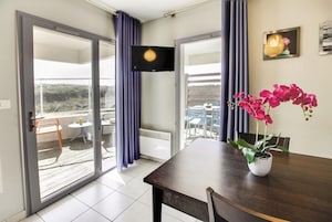 Une pièce comprenant une table à manger, une plante en pot, un téléviseur à écran plat et une porte-fenêtre coulissante donnant sur un espace extérieur avec une table et des chaises.