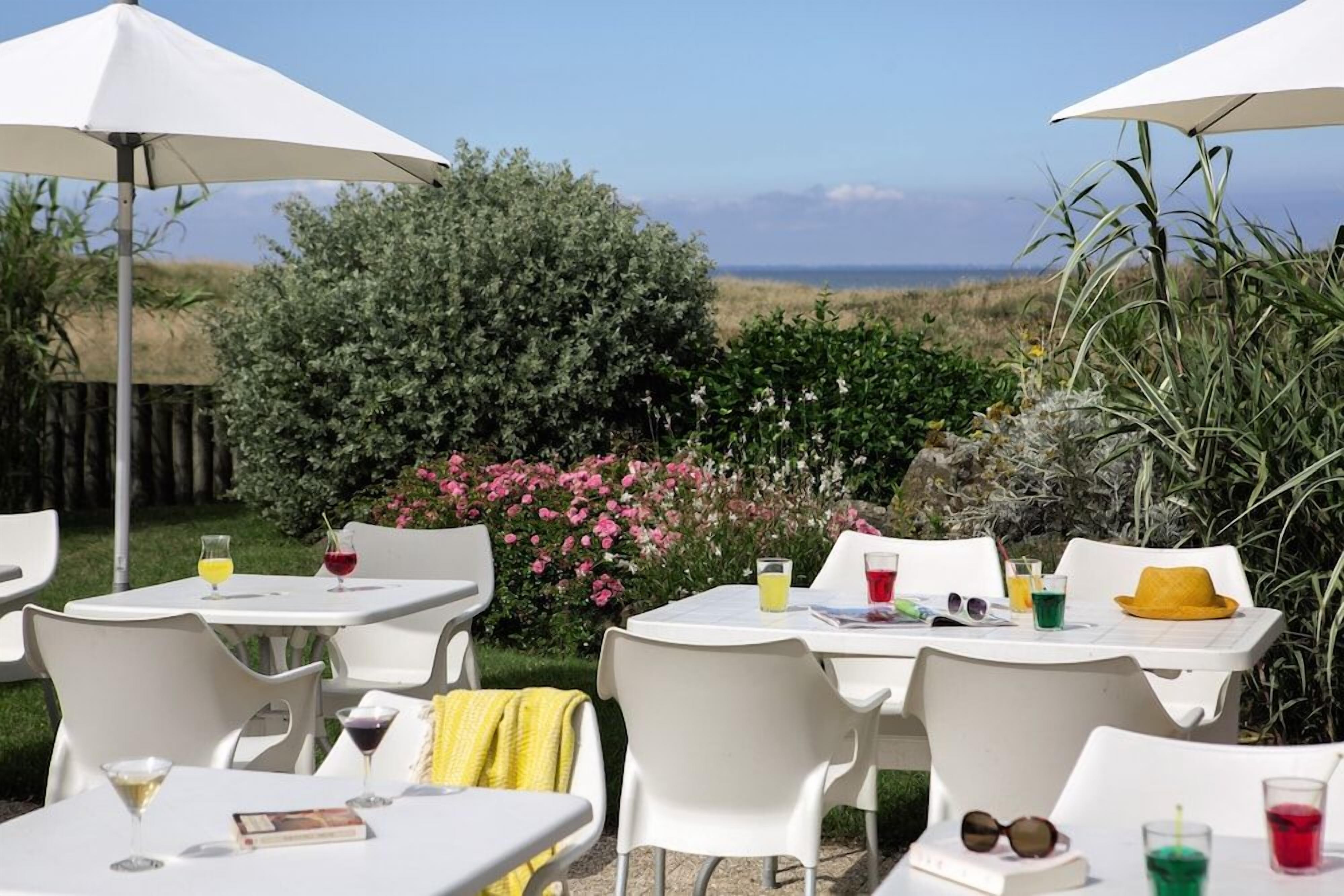 Een terras met witte tafels en stoelen, parasols en uitzicht op het landschap.