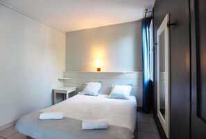 A hotel room with a bed, bedside table, lamp, and curtains. - Belambra Clubs Les Grands Espaces (Saint-Jean-de-Monts)