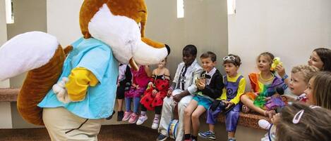 A person in a fox costume interacting with children seated on a bench.