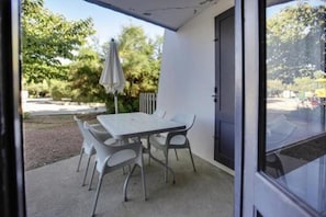 A covered patio area with a table and chairs, a door, and a view of the surrounding greenery. - Belambra Clubs Les Grands Espaces (Saint-Jean-de-Monts)