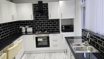 Una cocina moderna con armarios blancos, encimeras negras, horno empotrado y pileta de acero inoxidable.