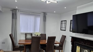 A living room with a sofa, a coffee table, a TV, a fireplace, and a dining area with chairs and a table. - Spacious 4-Bed House Near Manchester and Trafford Centre, Free Parking & WiFi (Partington)