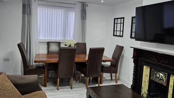 Una sala de estar con un sofá, una mesa de centro, un televisor, una chimenea y un comedor con sillas y una mesa.