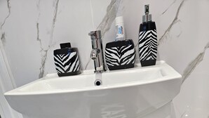A bathroom with a white sink, two faucets, a mirror, and a towel rack. - Spacious 4-Bed House Near Manchester and Trafford Centre, Free Parking & WiFi (Partington)