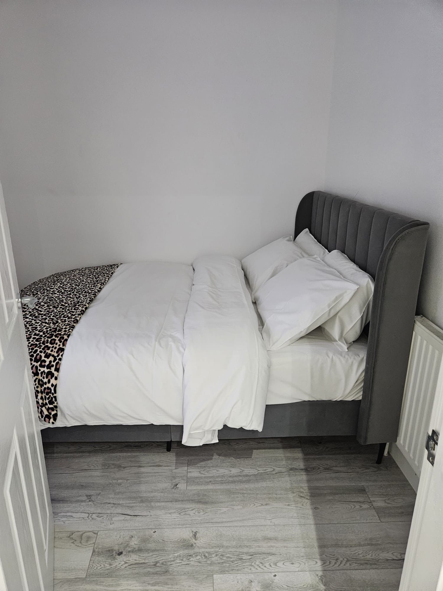 A single bed with a grey headboard and white bedding in a room with wooden flooring.