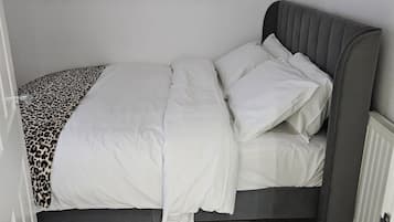 A single bed with a grey headboard and white bedding in a room with wooden flooring.