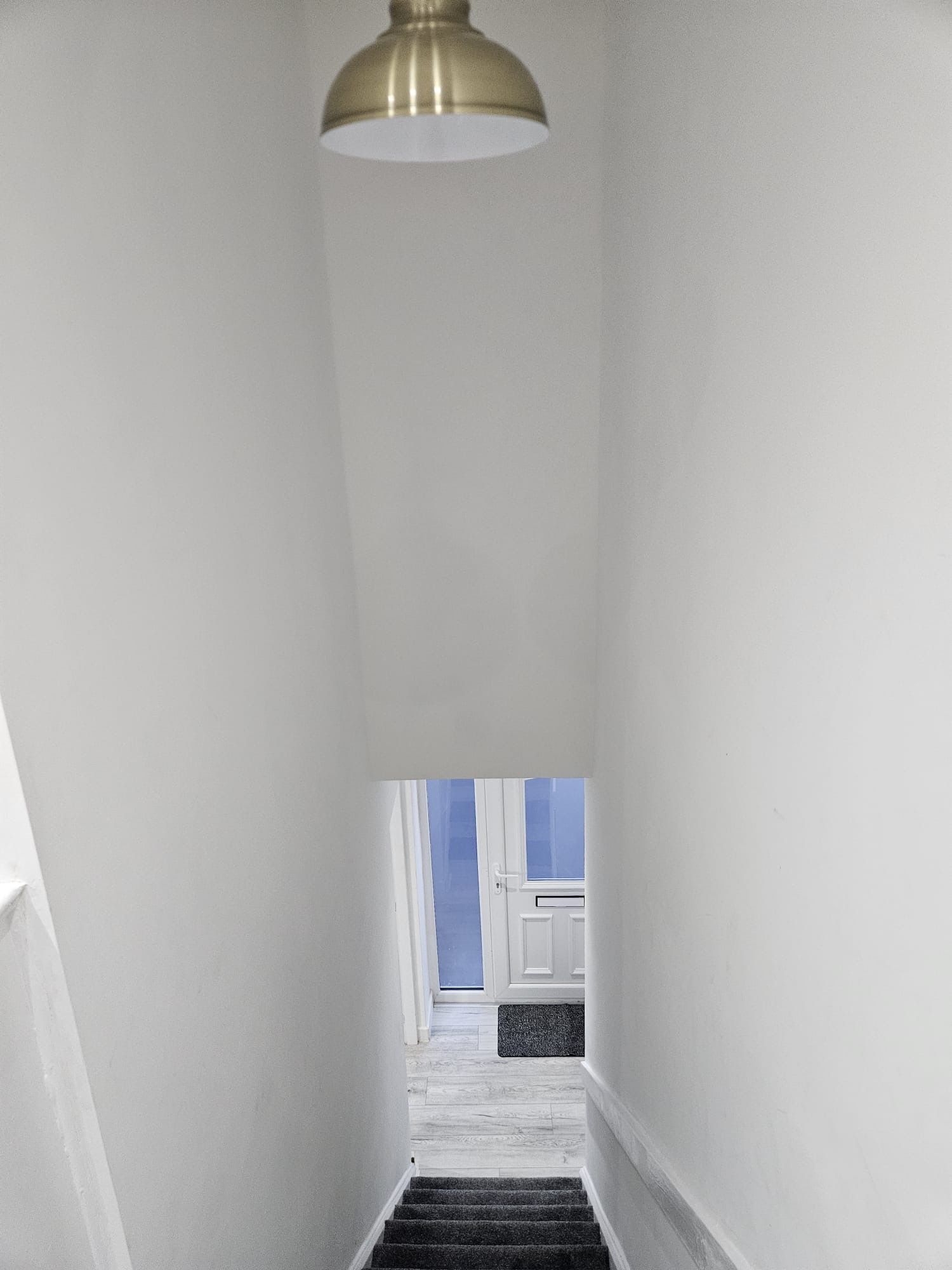 A narrow hallway with a staircase leading to a door with a window.
