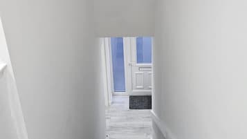 A narrow hallway with a staircase leading to a door with a window.