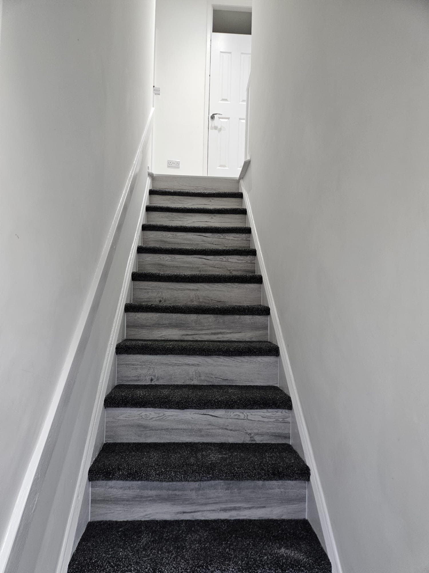 A staircase with wooden steps and carpeted risers, leading to a white door at the top.