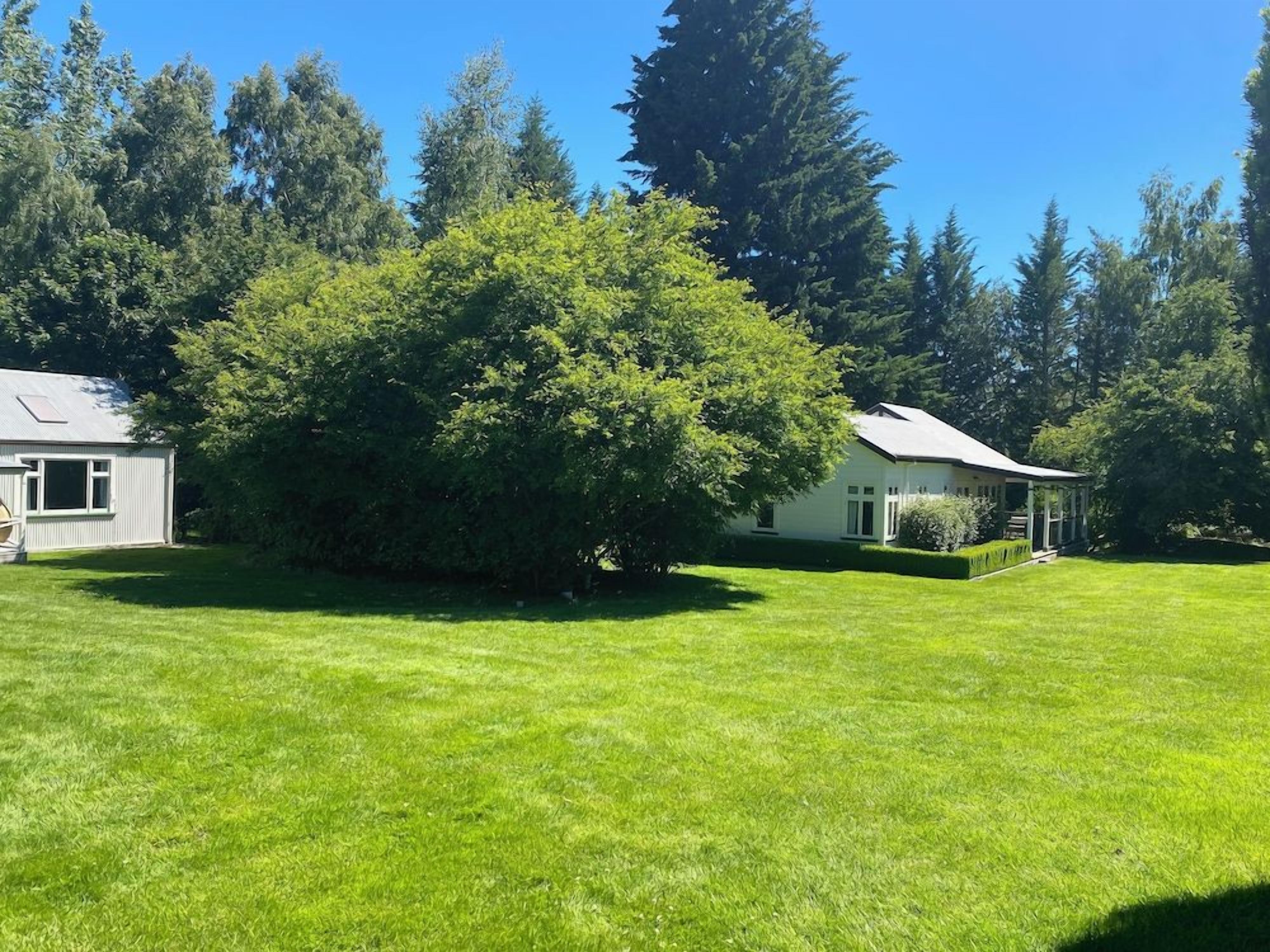 A residential property with a well-maintained lawn, a large tree, and a house with a sloped roof.