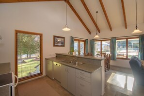 A kitchen with a central island, a dishwasher, and a sink. There are wooden beams on the ceiling and a window with blinds. - Willowbrook Country Apartments (Speargrass Flat)