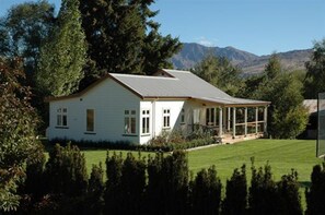 A single-story house with a covered porch, surrounded by a well-maintained lawn and dense trees. - Willowbrook Country Apartments (Speargrass Flat)