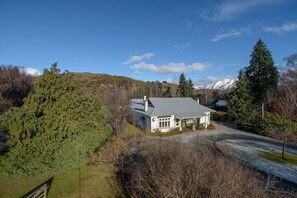 Ein Haus mit Schrägdach, umgeben von Bäumen und einem Berg im Hintergrund.