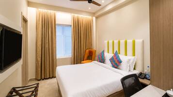 A hotel room with a bed, a desk, a chair, a television, and a ceiling fan.