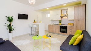A modern living room with a sofa, a TV, and a kitchen area with wooden cabinets and a stove. - Apartments A&M (Zupa dubrovacka)