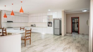 Een moderne keuken met witte kasten, een eethoek met houten stoelen en een koelkast.