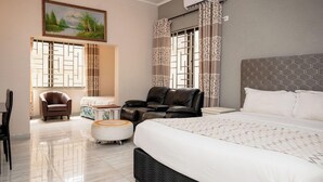 Een hotelkamer met een groot bed, twee leren fauteuils, een tafeltje en een schilderij aan de muur.