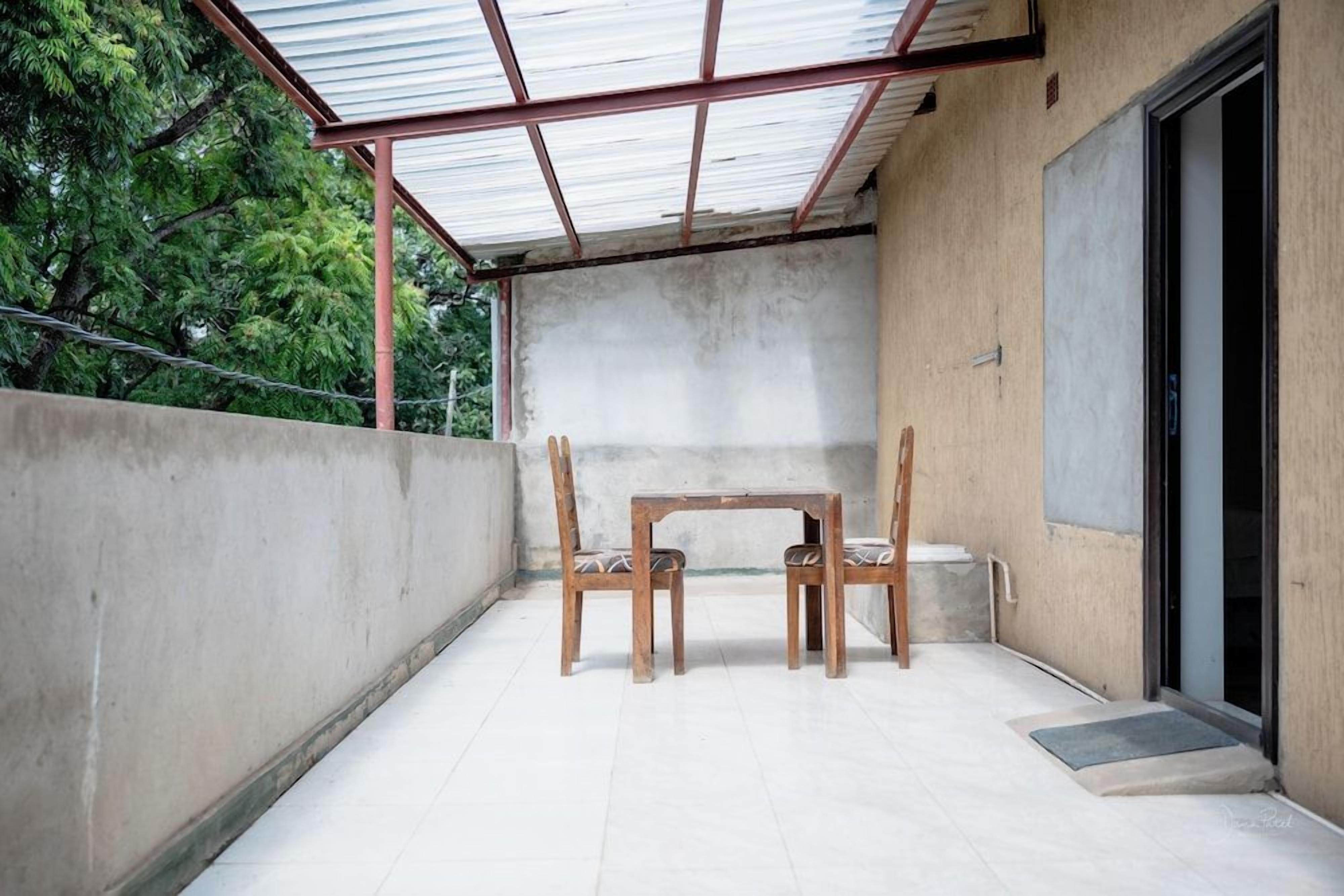 A covered outdoor area with a table and chairs, a concrete wall, and a door leading to a building.