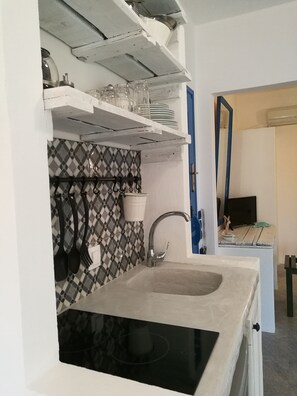 Eine Küche mit schwarzem Arbeitsplatz, einer Spüle und einer gefliesten Rückwand. Über der Spüle befinden sich Regale mit Tellern und Gläsern.