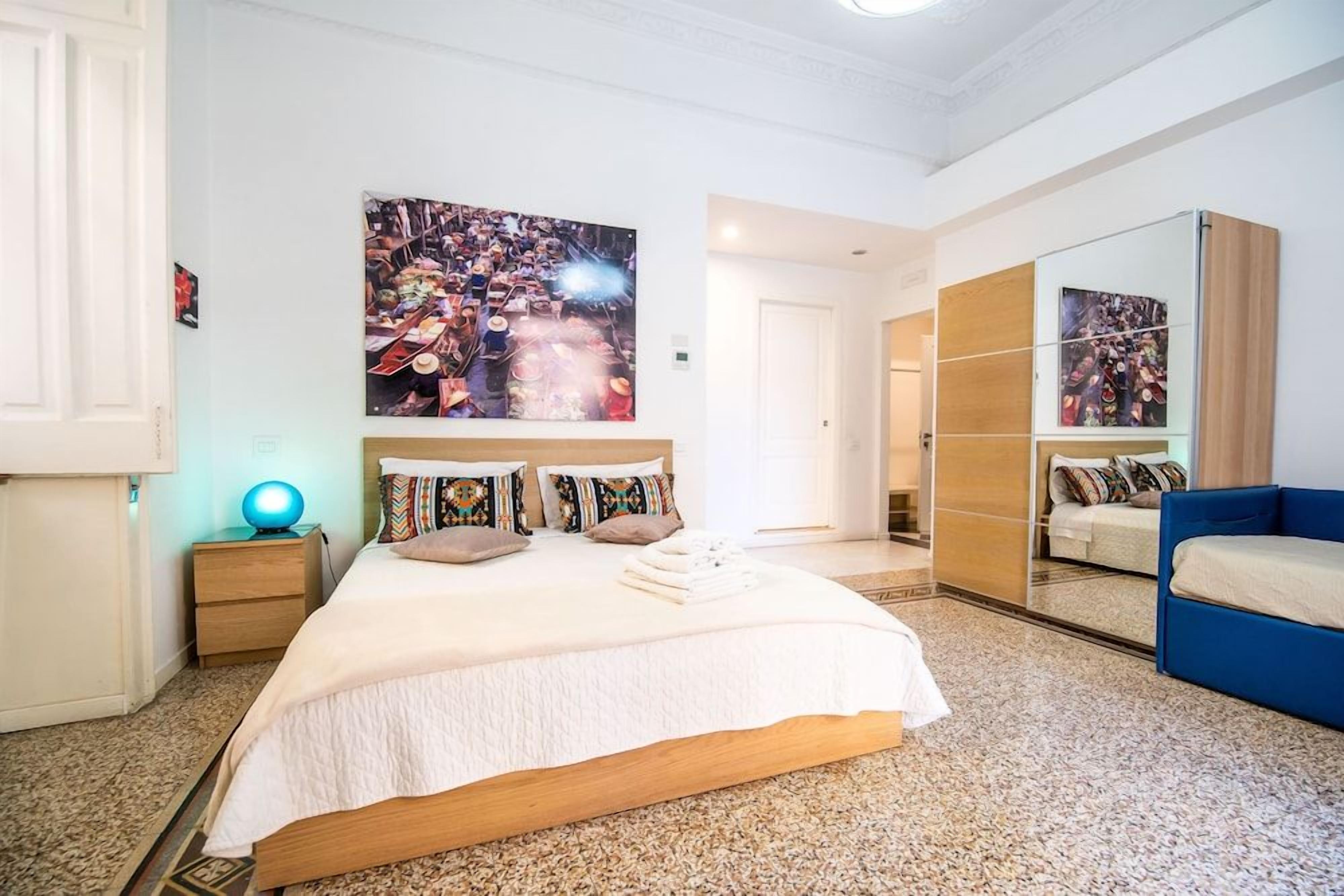A bedroom with a large bed, a nightstand, a blue chair, and a wardrobe.