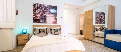 A bedroom with a large bed, a nightstand, a blue chair, and a wardrobe.