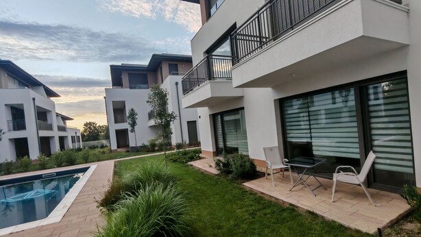 Un edificio residencial moderno con piscina, mobiliario exterior y un jardín bien cuidado.