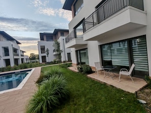 A modern residential building with a swimming pool, outdoor seating, and a well-maintained garden.