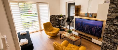 A modern living room with a flat-screen TV, yellow armchairs, a coffee table, and a stone accent wall.