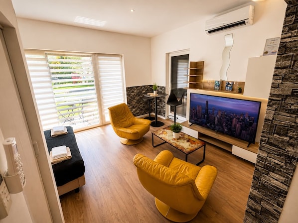 A modern living room with a flat-screen TV, yellow armchairs, a coffee table, and a stone accent wall.