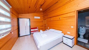 A wooden-paneled room with a bed, bedside table, and a red and white suitcase. - Ikiz Villas (Kemer)