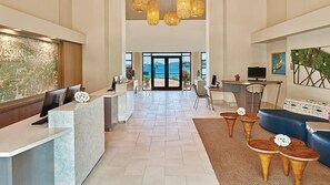 Un vestíbulo de hotel con una recepción, zona de estar y vistas al mar.