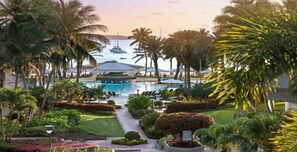 Un resort con piscina, palmeras y vistas a barcos en el agua.