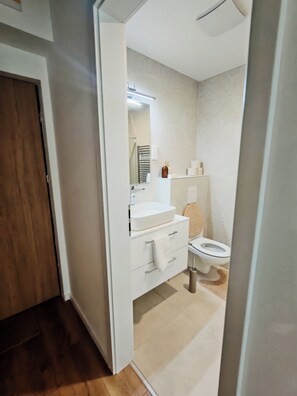 Un baño moderno con lavamanos, espejo y retrete blancos.