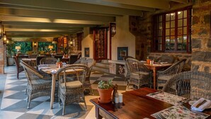Restaurante com mobiliário de vime, paredes de pedra e chão xadrez.